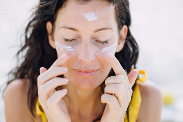woman wearing yellow eyes closed applying sunscreen to face outdoors AdobeStock 321197720.66ff2563b6349 Has DSM-Firmenich Put Us on a Path to a New U.S. Sunscreen Approval?