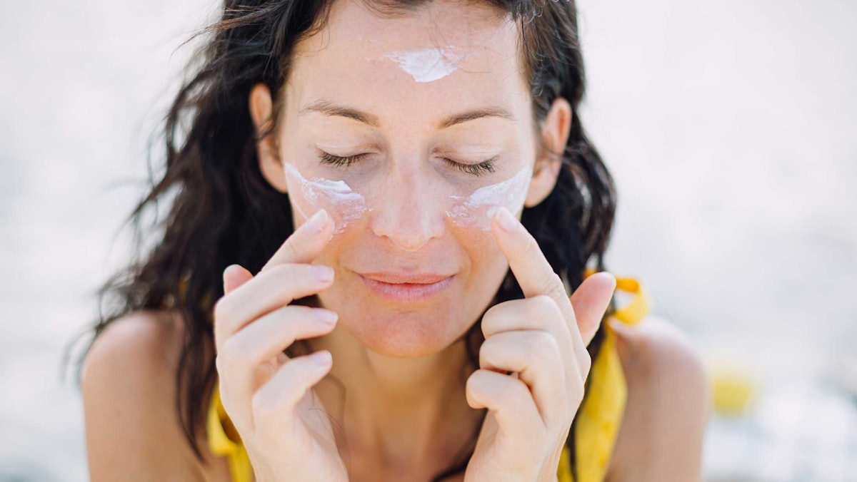 woman wearing yellow eyes closed applying sunscreen to face outdoors AdobeStock 321197720.66ff2563b6349 Has DSM-Firmenich Put Us on a Path to a New U.S. Sunscreen Approval?