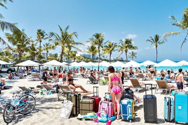 The Hottest Vacation Trends for 2025 Trendy travelers relaxing by the beach with luggage nearby.